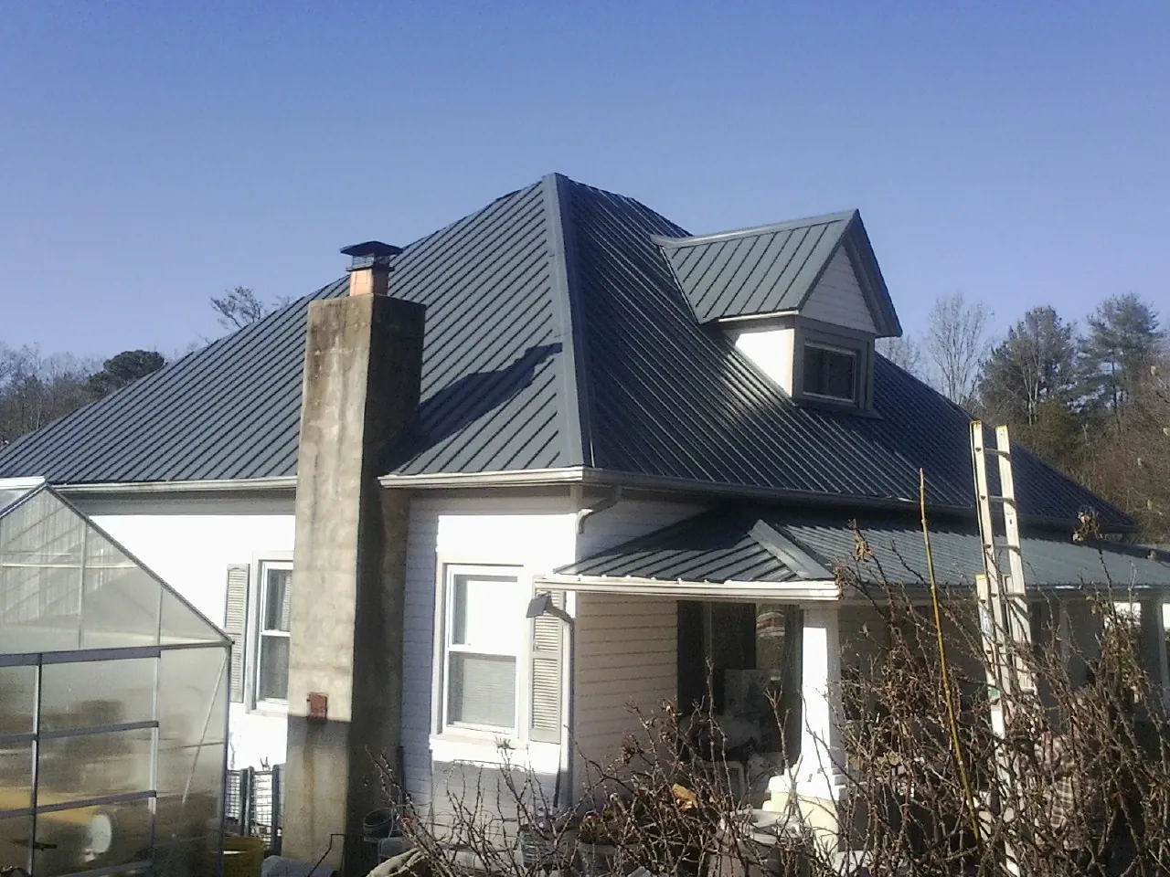 Dark blue standing seam metal roof on a white farmhouse with dormer — Slate & Tile Roof Repair by Roofing Brothers in Selden