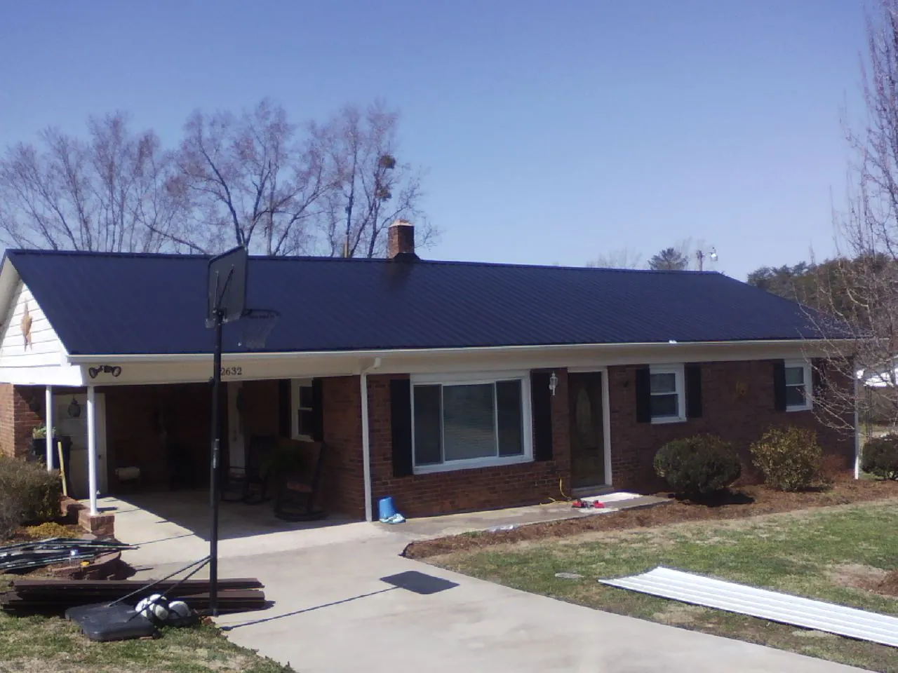 Finished dark blue metal roof on a brick ranch with a carport in Selden