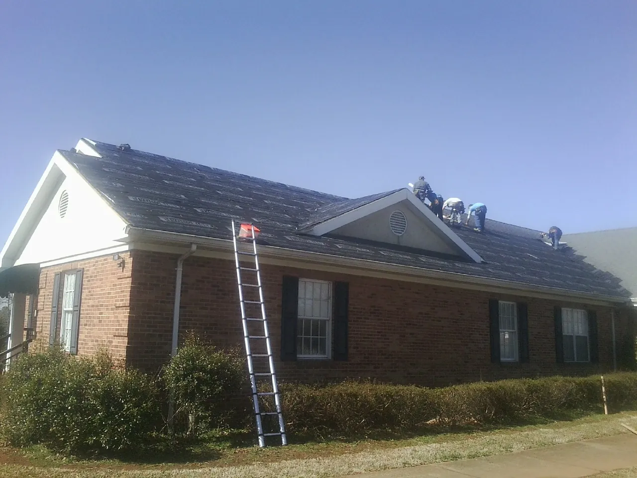 Crew tearing shingles off a brick ranch roof with a ladder set — Emergency Roof Repair work by our crew in Selden