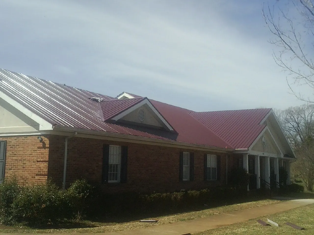 Red metal roof with gabled entries on a long brick building, from a Hail Damage Roof Repair job in Selden