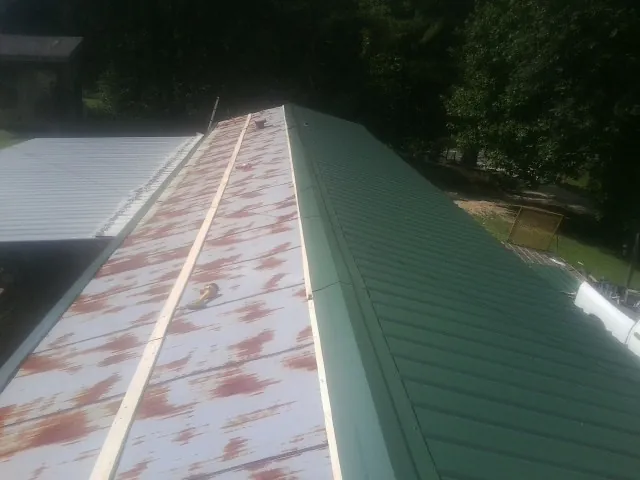 Old rusted panels beside newly installed green metal roofing — Wind Damage Roof Repair by Roofing Brothers in Selden