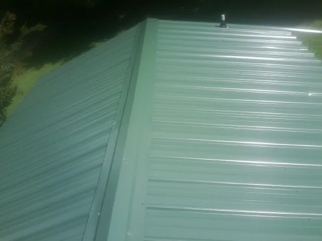 New green metal panels meeting at the ridge of a roof — Flat Roof Repair work by our crew in Selden