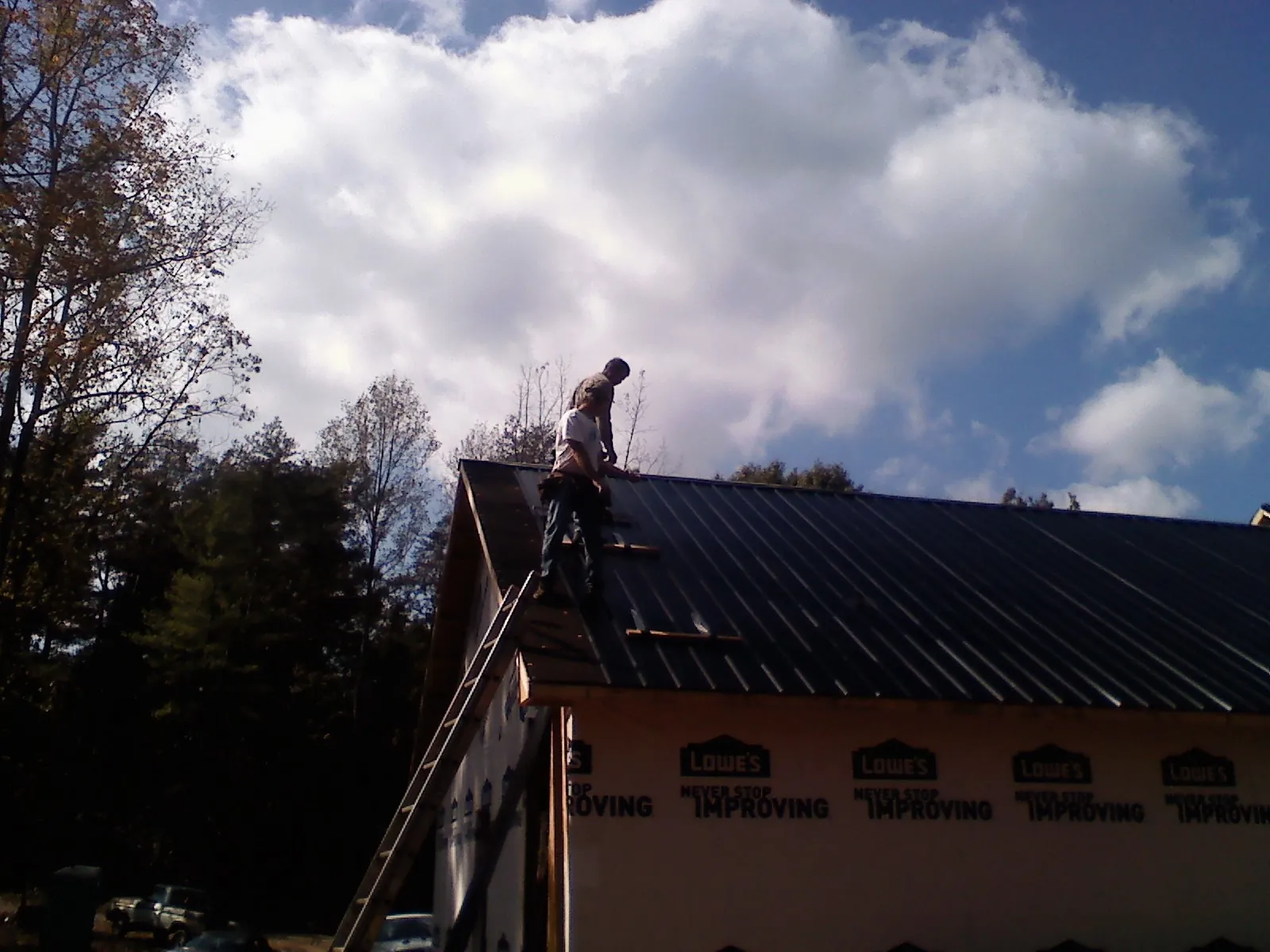 Roofer fastening dark metal panels high against a cloudy sky, from a Roof Inspection job in Selden