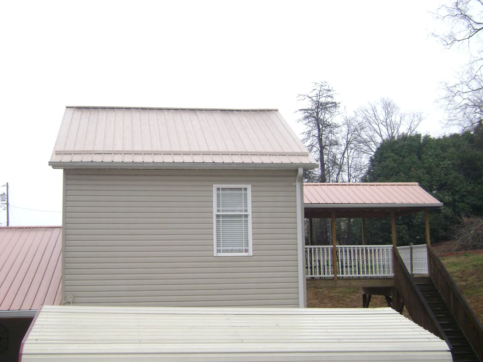 Tan metal roofs on a two story addition and attached porch, from a Roof Replacement job in Selden